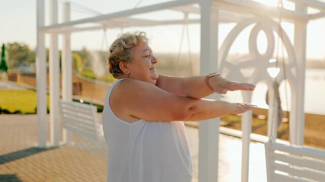 Joyful plus size pensioner swinging arms outside near the lake. fitness and healthy
