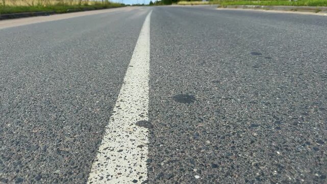 Empty asphalt road with white line marking stretching into distance, rural countryside setting with green grass and blue sky background