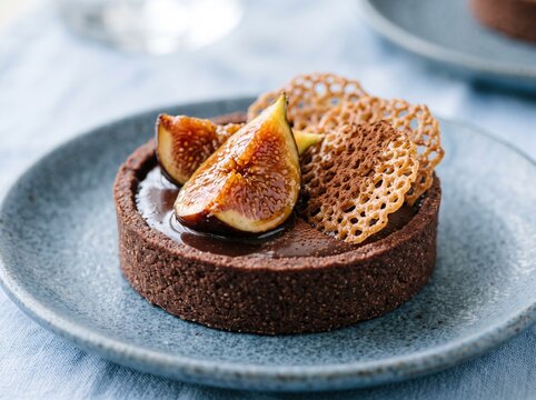Gourmet chocolate ganache tartlet garnished with fresh juicy fig slices and crispy lace cookies on a blue plate