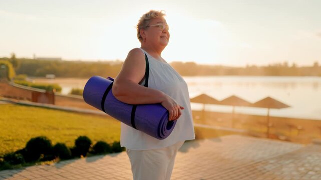 Authentic mature person holding yoga mat enjoying sunrise lake. fitness and healthy