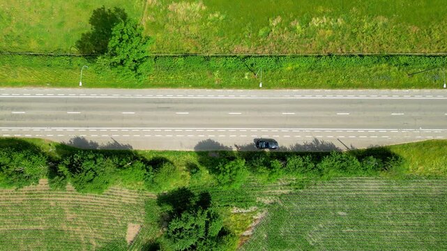 Aerial Top-Down View of Red Car Driving on a Country Road Through Green Landscape