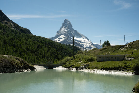 Matterhorn mountain peak rising above a green tinged reservoir with surrounding lush alpine landscape