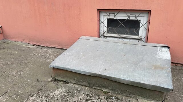 Basement window with metal cover, stucco wall and grated vent, stainless sheet protecting cellar well from rain, concrete ledge