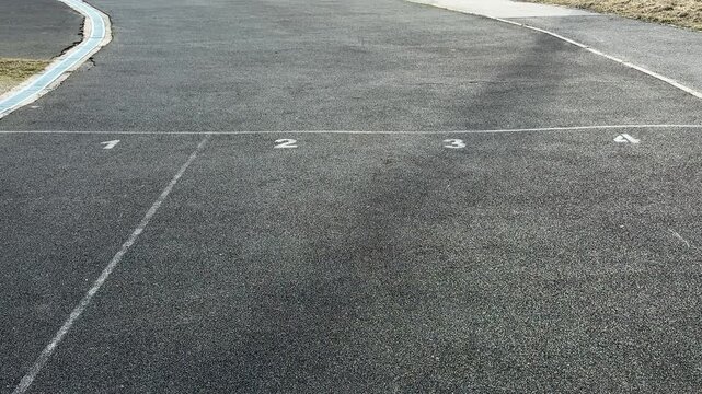 Close-up running track asphalt surface curve showing granular rubber texture, faded lane marking and grassy verge, empty prerace