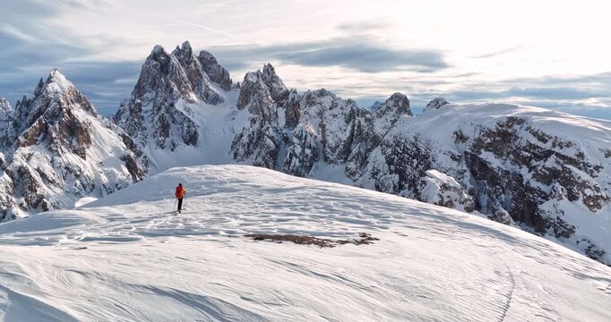 Cinematic orbital drone shot circling a backcountry skier crossing a snowy ridge in the Dolomites revealing dramatic alpine peaks pristine winter scenery and breathtaking mountain landscapes.