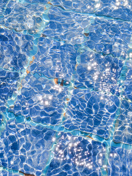 Crystal clear blue swimming pool water surface aerial view with sparkling light reflections and ripple texture