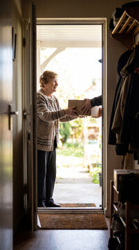 Smiling senior woman receiving parcel from courier at open front door, authentic active aging concept showing independence confidence value value value value value value value value