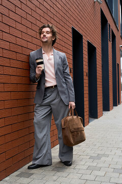 Stylish man with curly hair enjoying coffee while walking down a vibrant city street