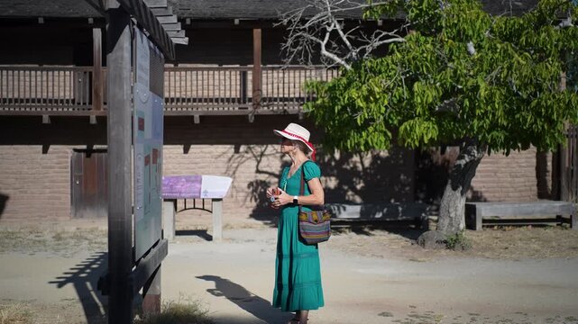 Mature woman smiles as she walks through Casa Grande, home of General Vallejo, reading about its history on a bright morning.