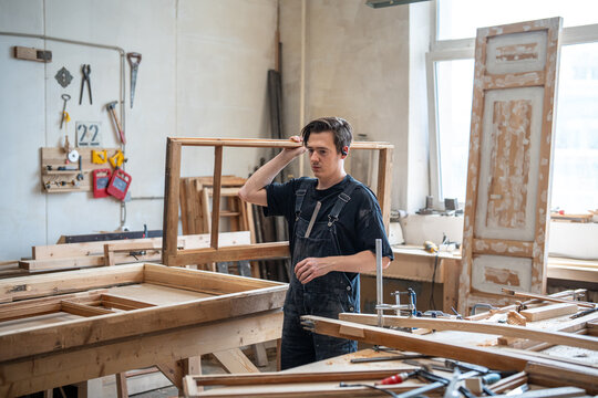 Workday in restoration workshop:, master carpenter carries part of antique wooden window frame, working process of restoration and reconstruction, craftsmanship and small woodworking business.