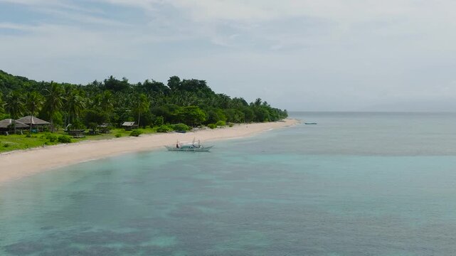 Ocean waves crashing on white sand. Boat over clear turquoise water with corals. Santa Fe, Tablas, Romblon. Philippines.