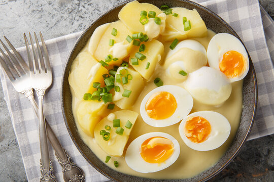 Close-up of hard-boiled eggs in mustard sauce with a side dish of boiled potatoes in a plate on the table. Horizontal top view from above