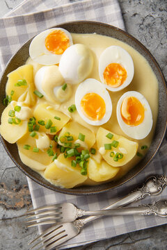 Senfeier German eggs in mustard sauce with a side dish of boiled potatoes close-up in a plate on the table. Vertical top view from above