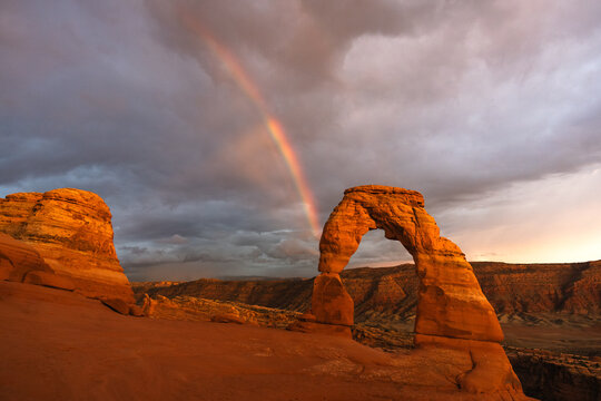 Rainbow and dark clouds behind Delicate Arch at Arches National Park, Utah