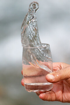 Hand holds glass with water splashing upward