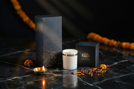 Luxury black gift boxes with gold branding a lit brass diya a white scented candle and vibrant marigold flower petals arranged beautifully for a festive Indian Diwali celebration