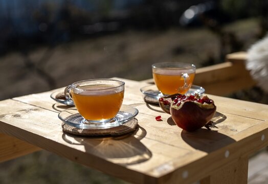 Two cups of herbal tea and sliced pomegranate on a wooden table outdoors