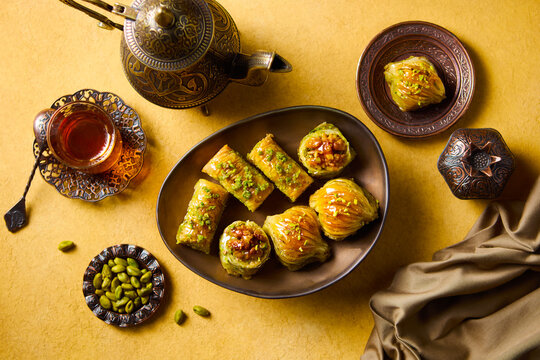 Traditional oriental sweets ramadan celebration food featuring sweet baklava dessert and vintage teapot. Yellow background. Top view.