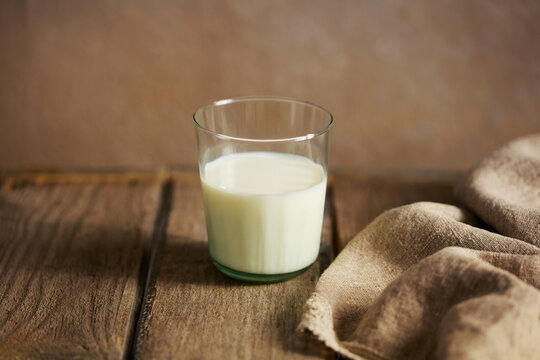 Pure milk in a glass with linen cloth and wooden surface. Brown background. Close up.