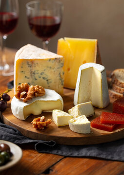 Aesthetic close up rustic cheese board with quince paste walnuts and wine bokeh. Brown wooden background. Close up.