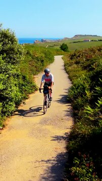 Instagram Reels 9:16 video of a cyclist riding down a scenic paved path surrounded by nature with the sea in the background. Healthy lifestyle, outdoor fitness, cycling workout and active living conce