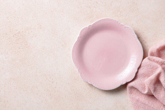 Empty pink ceramic plate with linen napkin on beige textured background. Close up. Top view. Copy space.