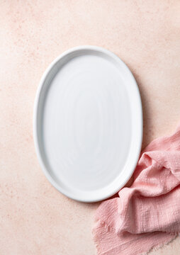 Empty white oval platter with pink napkin on beige background. Copy space. Top view.