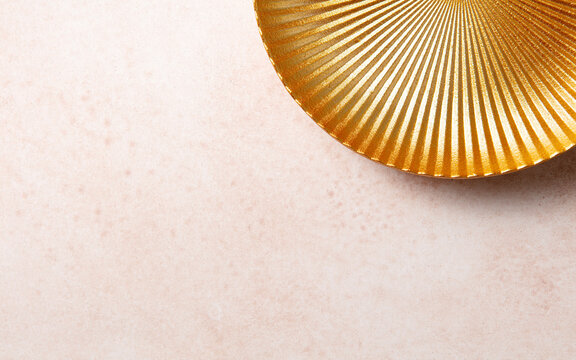 Flat lay view of golden ribbed platter edge on pastel pink concrete surface. Minimalist abstract background template for holiday greeting or luxury product layout
