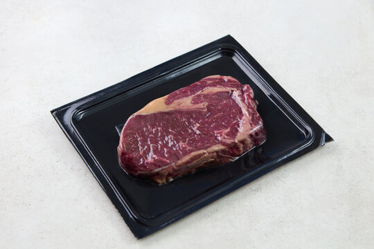 Fresh uncooked marbled ribeye steak vacuum sealed on bright texture tabletop side view. Grey background. Close up.