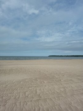 Minimalist landscape of a vast empty sandy beach and calm sea under a gloomy cloudy sky