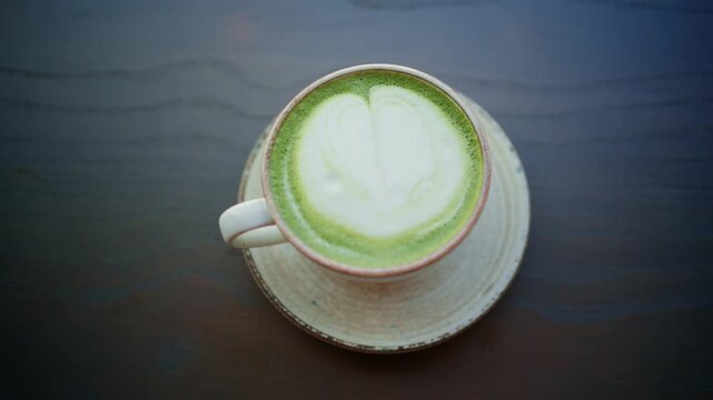 Top view of refreshing warm green matcha tea drink with beautiful milk foam art in ceramic cup.