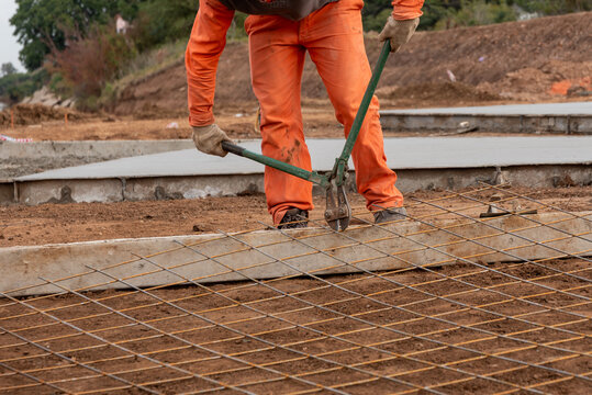 Construction worker cutting steel rebar mesh with manual bolt cutter on paving site