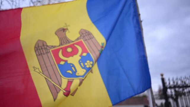 Moldovan flag waves proudly against a cloudy sky and modern building facade dynamic motion.