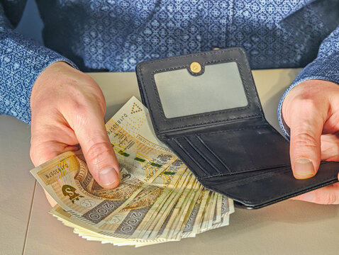 Man putting 200 Polish Zloty PLN banknotes into black leather wallet, financial savings concept