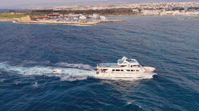 Aerial view of white motor yacht cruising on deep blue sea near coastline of Paphos city in Cyprus.