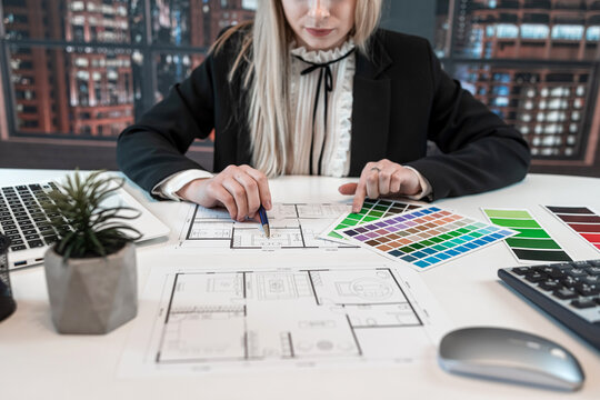 Young caucasian female engineer or designer drawing a blue print with color catalog