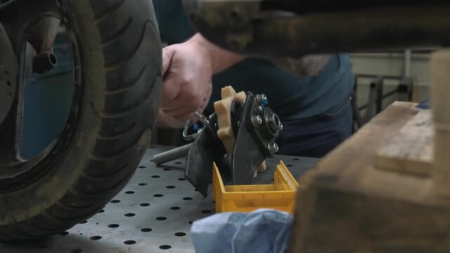 An engineer assembles a transmission mechanism with a bearing. He inserts bolts into the grooves, installs washers, and tightens the nuts with a hex wrench. Then checks the mechanism's functionality