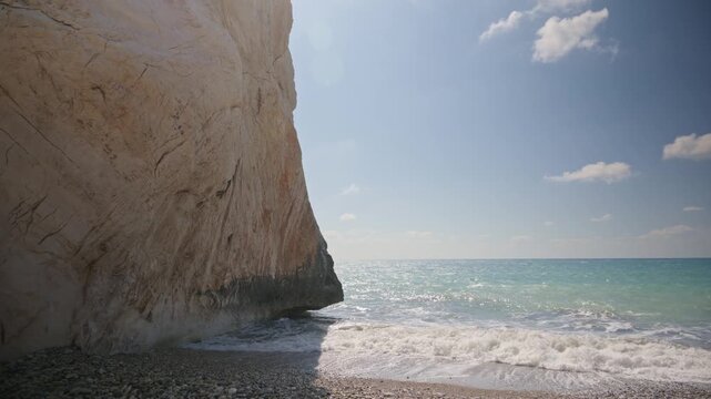 Ocean waves crash against a white rocky cliff on a sunny day with a blue sky.
