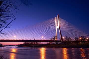 Fototapeta premium A modern cable-stayed bridge over the river, illuminated by lights.