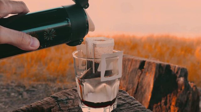 Hand Pouring Hot Water Slowly into Portable Drip Coffee at the Lakeshore Campsite