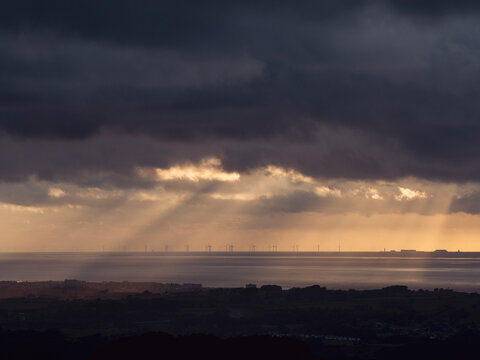 Dramatic coastal sunset with offshore wind turbine silhouettes