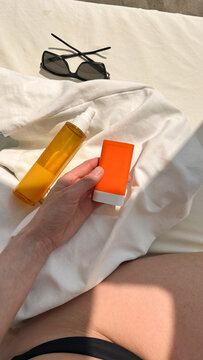 A hand holds sunscreen and body oil on a beach towel
