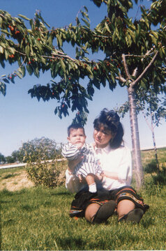 Mother holding baby under cherry tree enjoying summer day