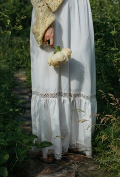 Anonymous woman in white skirt with flower in hand