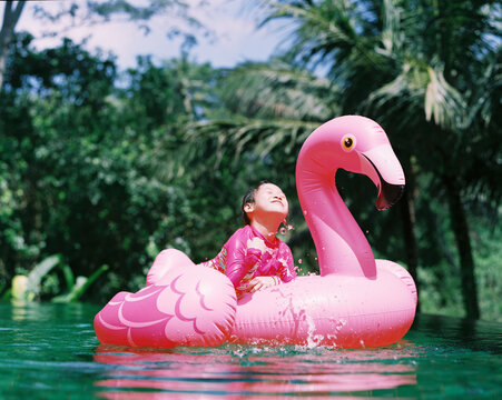 Chinese girl happily playing in a pool with a pink flamingo swim ring