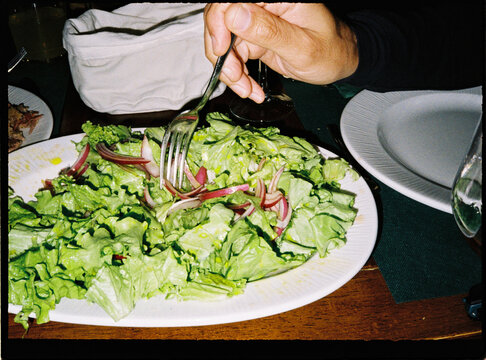 Hand eating healthy green salad with red onion