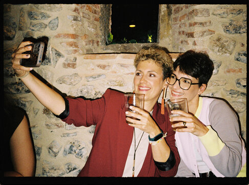 Two women taking a selfie enjoying drinks at a party