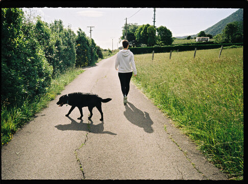 Woman walking black dog on country road in summer