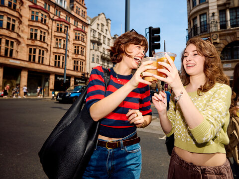 Women joyfully toast with takeaway drinks the city street.