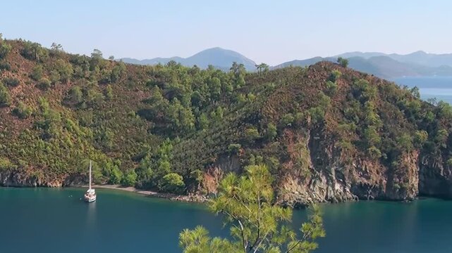 A pristine sailboat rests peacefully in a secluded Fethiye Turkey bay, surrounded by vibrant green hills and towering rocky cliffs under a clear blue sky. This idyllic haven offers a perfect escape.